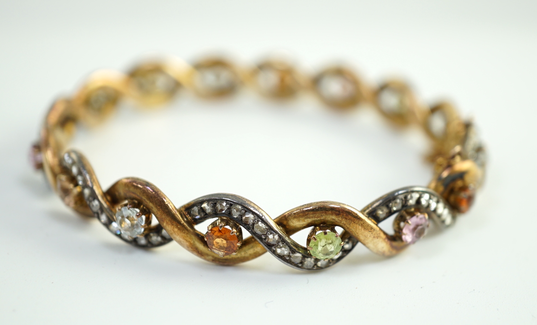 A late 19th/early 20th century French 18ct gold and silver rose cut diamond and multi gem set spiral hinged bangle